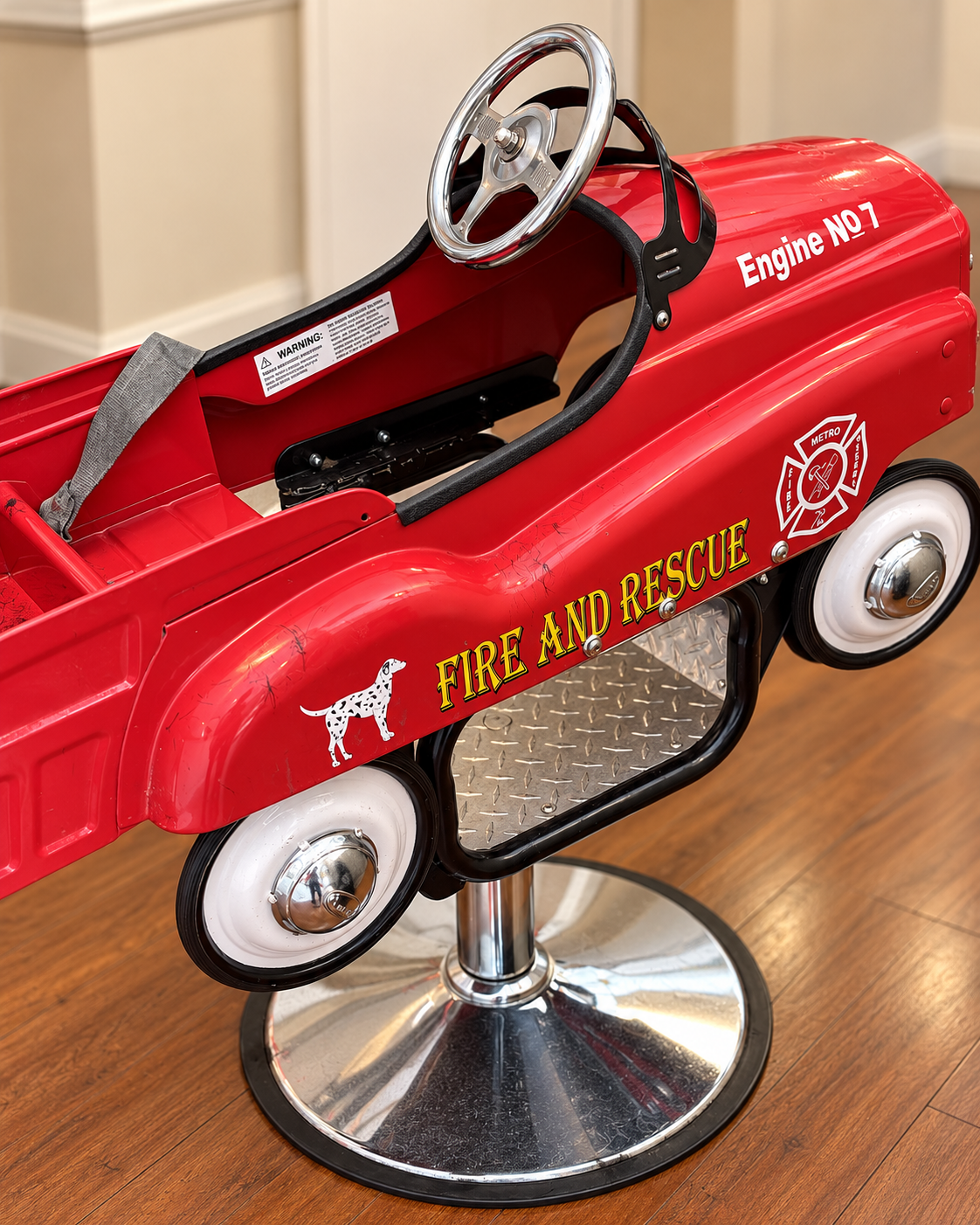 The empty red fire-truck haircut chair with a steering wheel and chrome pedestal